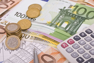 Das Bild zeigt Geldscheine und Münzen in Euro, sowie einen Taschenrechner und Diagramme für finanzielle Berechnungen.