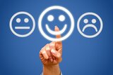Eine Hand zeigt auf ein leuchtendes Smiley-Gesicht, umgeben von neutralen und traurigen Gesichtern. Symbolisiert Stimmung oder Feedback.