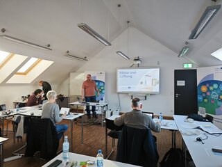 In einem modernen Seminarraum präsentiert eine Person über das Thema Klimatisierung und Lüftung. Teilnehmer sind aktiv beteiligt.